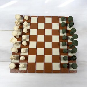 May include: A novelty chess set with mushroom-shaped pieces in off-white and dark green. The chessboard has a brown and cream checkered pattern. The pieces are arranged on the board, ready for play.