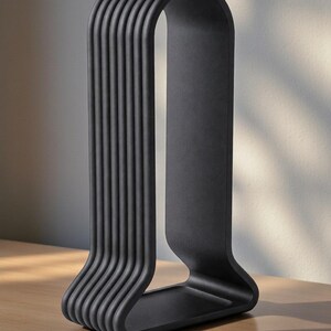 May include: A matte black, modern sculpture with a unique design. The sculpture features a series of vertical, curved lines that connect at the top and bottom, creating an arch shape. It is placed on a wooden surface.