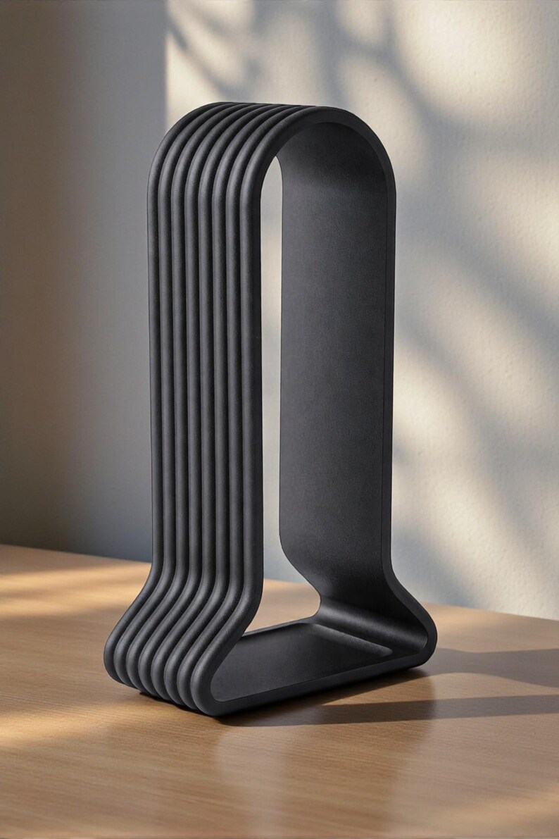 May include: A matte black, modern sculpture with a unique design. The sculpture features a series of vertical, curved lines that connect at the top and bottom, creating an arch shape. It is placed on a wooden surface.