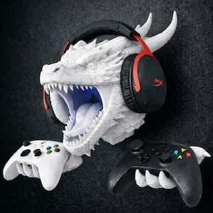 May include: A white dragon head wall mount with a headset and two game controllers. The dragon's mouth is open, revealing teeth and a blue interior. The headset is black and red. One controller is white, the other is black.