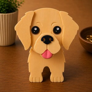 May include: A golden retriever puppy figurine with large black eyes, a black nose, and a pink tongue. The dog has floppy ears and is standing upright. The figurine is made of a light tan material and is on a wooden surface.
