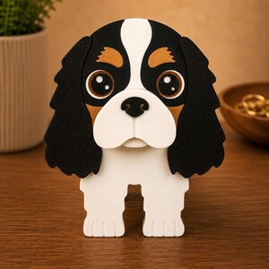 Pu&ograve; includere: Statuetta decorativa a forma di cane Cavalier King Charles Spaniel. Il cane ha una combinazione di colori nero, bianco e marrone con grandi occhi espressivi. La statuetta &egrave; su una superficie di legno.