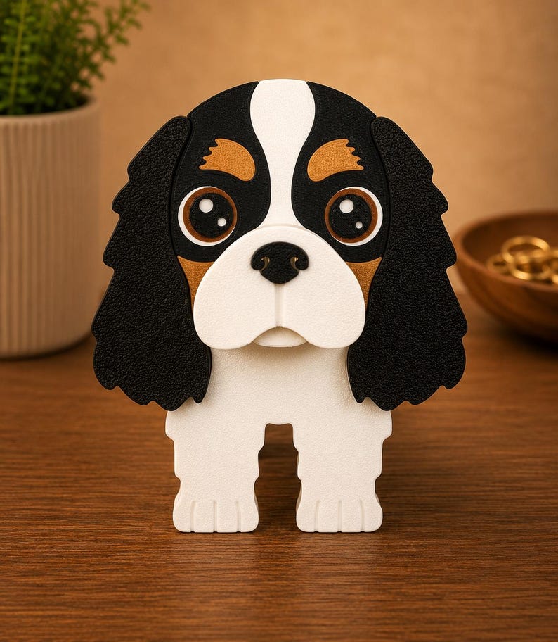 Pu&ograve; includere: Statuetta decorativa a forma di cane Cavalier King Charles Spaniel. Il cane ha una combinazione di colori nero, bianco e marrone con grandi occhi espressivi. La statuetta &egrave; su una superficie di legno.