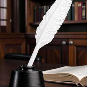 May include: A white feather quill pen is placed in a black inkwell on a dark wooden desk. An open book is visible in the background, with a wooden bookshelf filled with books. The scene evokes a classic writing or study setting.