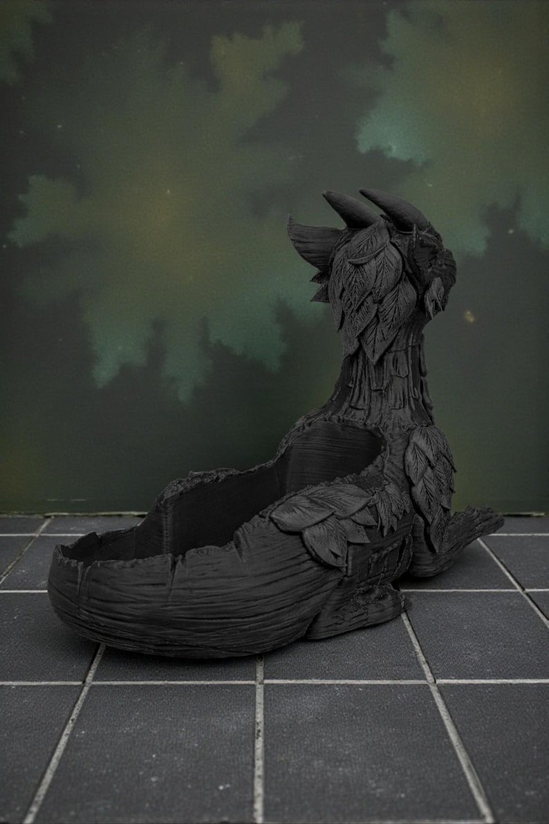 May include: A black dragon-shaped planter with a textured surface. The planter features a detailed design with leaf-like accents and a large opening for plants. The dragon's head is upright, and the overall design is dark and mysterious.