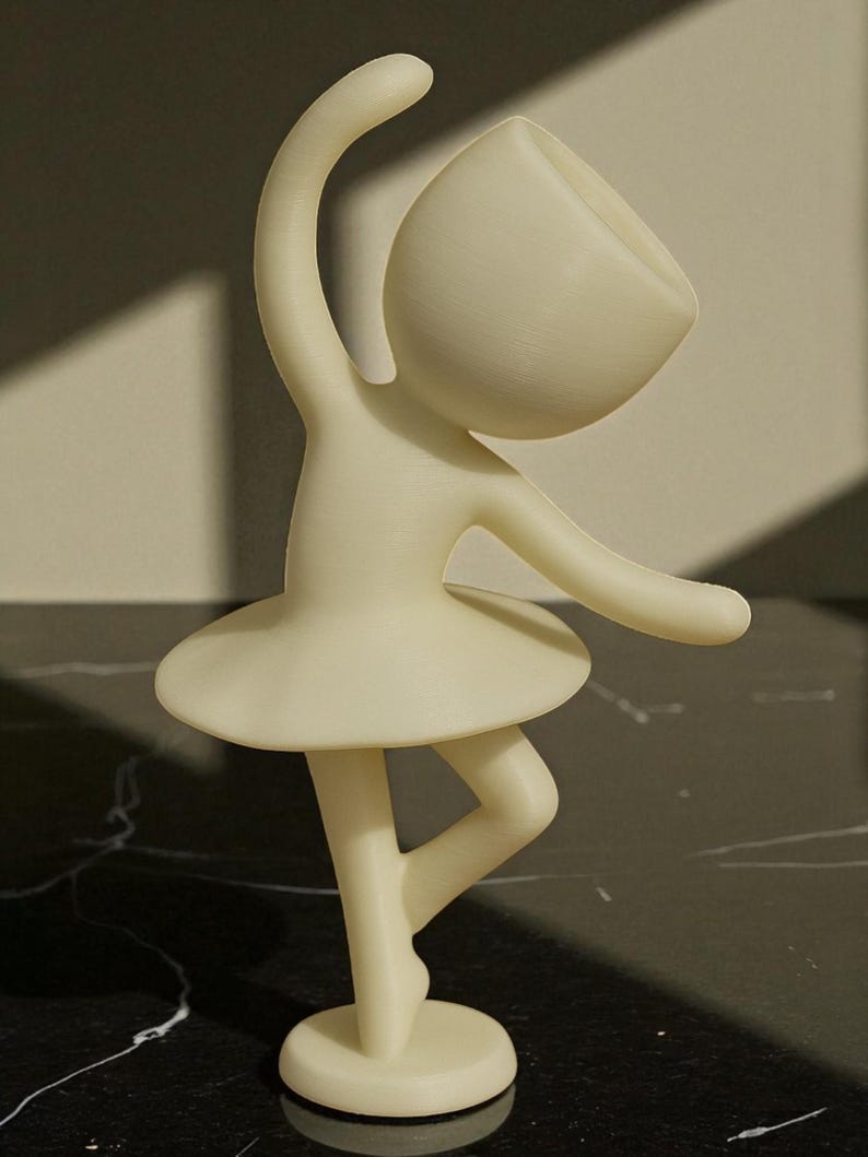 May include: A cream-colored figurine of a ballerina in a graceful pose. The figure has a rounded head, arms outstretched, and a tutu. The figurine is standing on one leg, with the other bent.
