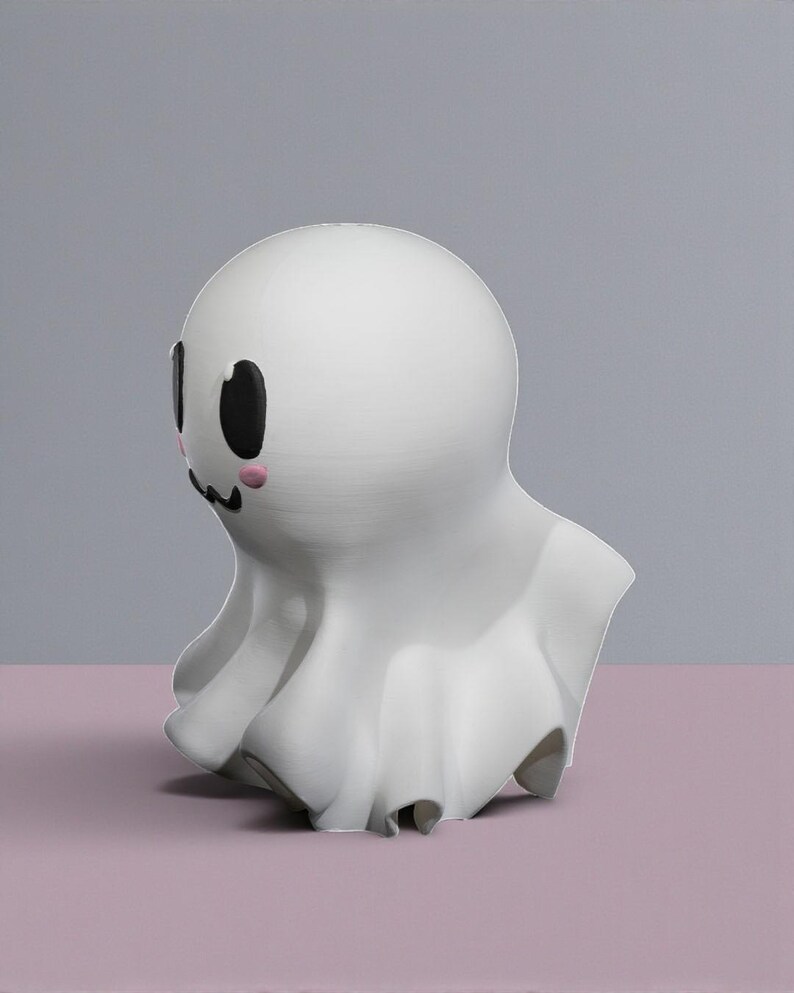 May include: A white ghost figurine with a rounded head and a draped body. The ghost has black oval eyes, a small black mouth, and pink blush marks on its cheeks. The figurine is set against a gray and pink background.