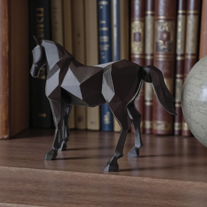 May include: A dark gray geometric horse sculpture with a faceted design. The horse figurine is displayed on a wooden shelf in front of a backdrop of antique books. The sculpture has a modern, minimalist aesthetic.