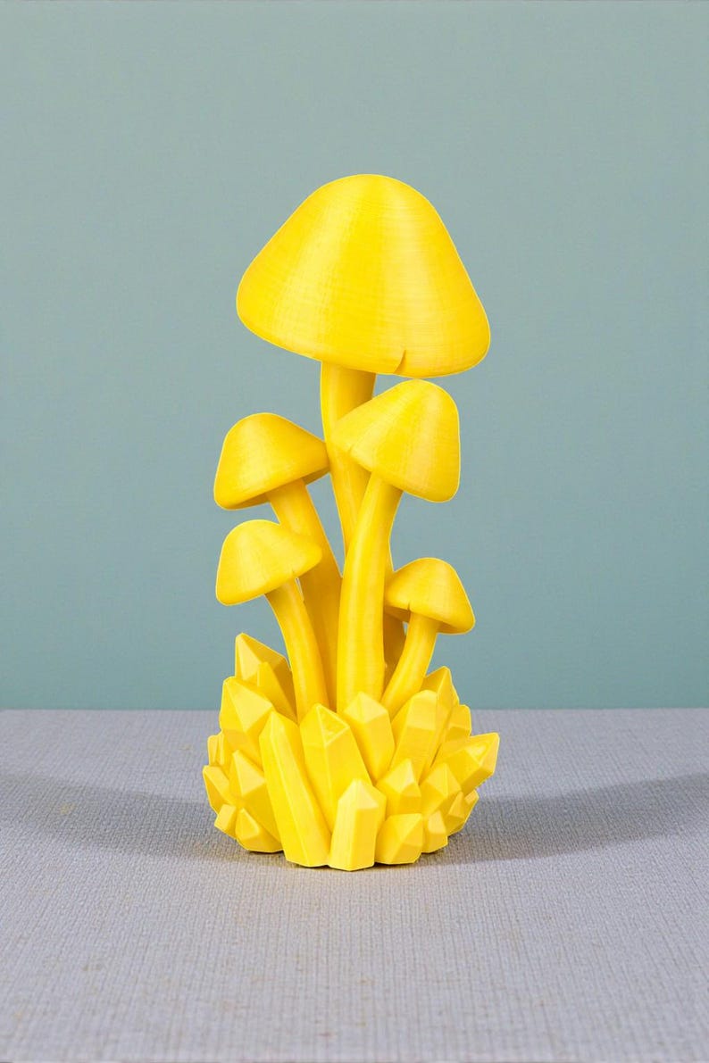 K&ouml;nnte beinhalten: Eine leuchtend gelbe Pilzskulptur mit mehreren Pilzkappen und -stielen. Die Basis ist eine Ansammlung gelber kristallartiger Formen. Die Skulptur steht vor einem hellblauen Hintergrund.