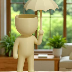 May include: A cream-colored figurine of a person holding an umbrella. The figure has a large, open head, designed to hold plants. The umbrella is also cream-colored, and the figure is standing on a wooden surface.