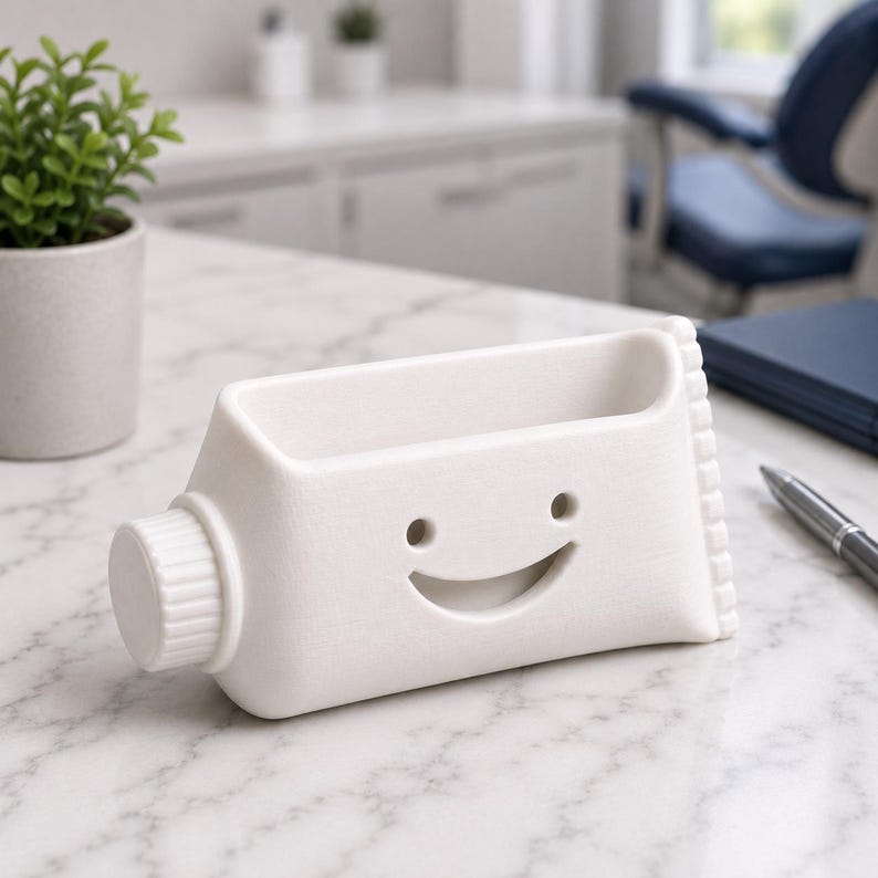 Pu&ograve; includere: Un organizer da scrivania in ceramica bianca a forma di tubetto di dentifricio, con un volto sorridente. Ha un vano rettangolare per penne e un tappo a vite. Il design &egrave; giocoso e moderno.