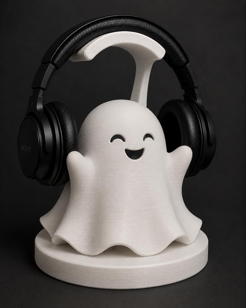 May include: A white 3D-printed headphone stand shaped like a smiling ghost, holding black headphones. The stand has a round base and a curved top to hold the headphones. The headphones are black with the brand name "SONY" visible.
