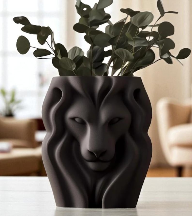 May include: A dark grey ceramic vase featuring a lion's face design, filled with green leafy branches. The lion's face is sculpted with detailed features. This decorative vase is a home accent, suitable for displaying flowers or foliage.