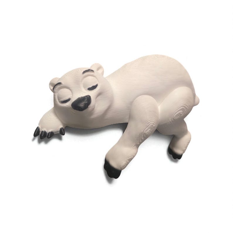 May include: A white polar bear figurine in a relaxed pose, lying on its side with its eyes closed. The bear has black paws and a black nose. The figurine is a decorative item.