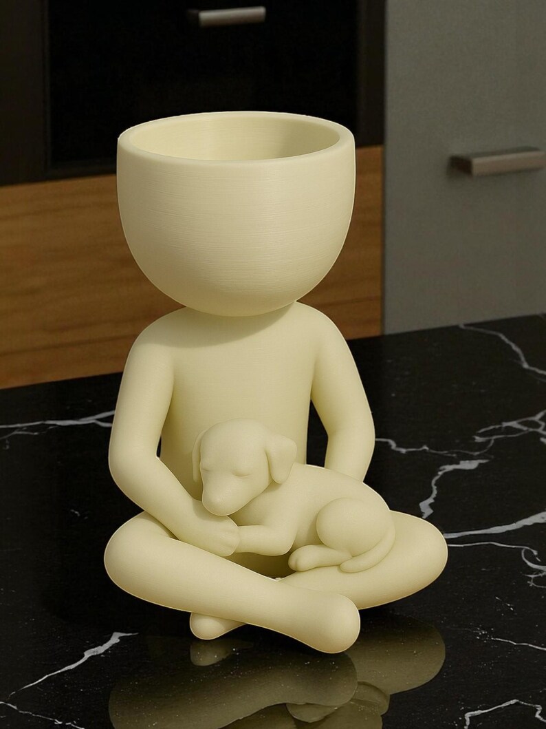 May include: A cream-colored figurine of a person seated with legs crossed, cradling a sleeping puppy. The figure has a large, open head, designed to hold small plants or items. The figurine is on a black, marble-like surface.