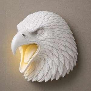 May include: A white eagle head wall sculpture with an open beak, revealing a warm, yellow interior. The sculpture features detailed feather textures and is mounted on a neutral-toned wall. The eagle's eye is visible, and the overall design is a decorative wall accent.