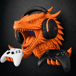 May include: A bright orange dragon head wall mount featuring textured scales and an open mouth. The dragon wears black and orange over-ear headphones and uses its clawed hands to hold a white game controller and a black game controller.