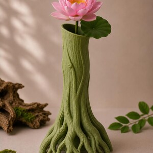 May include: A green vase shaped like a tree trunk, with roots at the base and a flared opening. A pink lotus flower with a yellow center and a green leaf are in the vase. The vase has a textured surface, and the background is a neutral color.