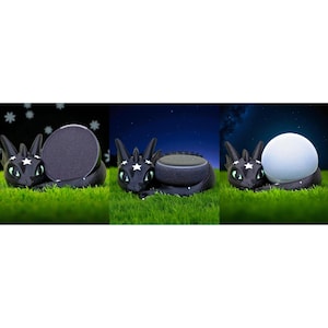 Puede incluir: Soportes de altavoz con forma de dragón negro con detalles de estrellas y ojos verdes, sobre hierba verde. El dragón sostiene un altavoz redondo, un disco negro redondo y una esfera blanca. El fondo muestra una noche estrellada.