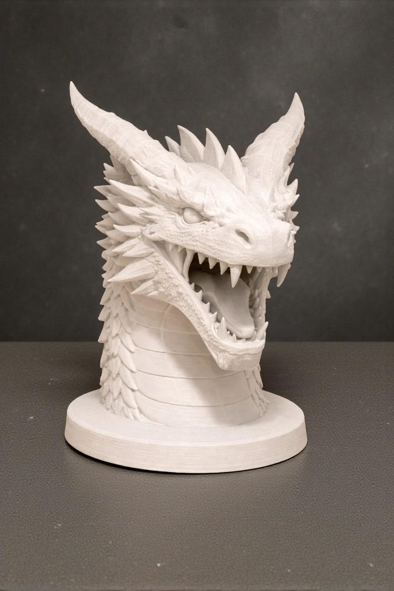 May include: A white dragon head sculpture with open mouth, sharp teeth, and detailed scales. The dragon has prominent horns and a spiked ridge along its back. The sculpture is mounted on a circular base, showcasing a fantasy theme.