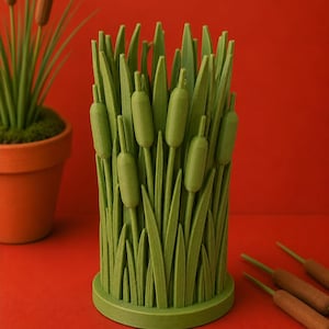 May include: A green decorative vase shaped like cattails and reeds. The vase features a cylindrical design with detailed leaves and cattail heads. The vase is set against a red background, with a potted plant and additional cattails visible.