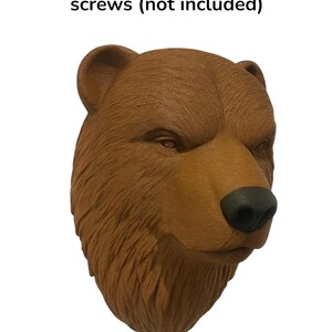 Puede incluir: Escultura de cabeza de oso marr&oacute;n con superficie texturizada. El oso tiene una nariz negra y una textura de pelaje detallada. El texto "mounts to wall with screws (not included)" est&aacute; encima de la cabeza del oso. Pieza decorativa para montaje en pared.