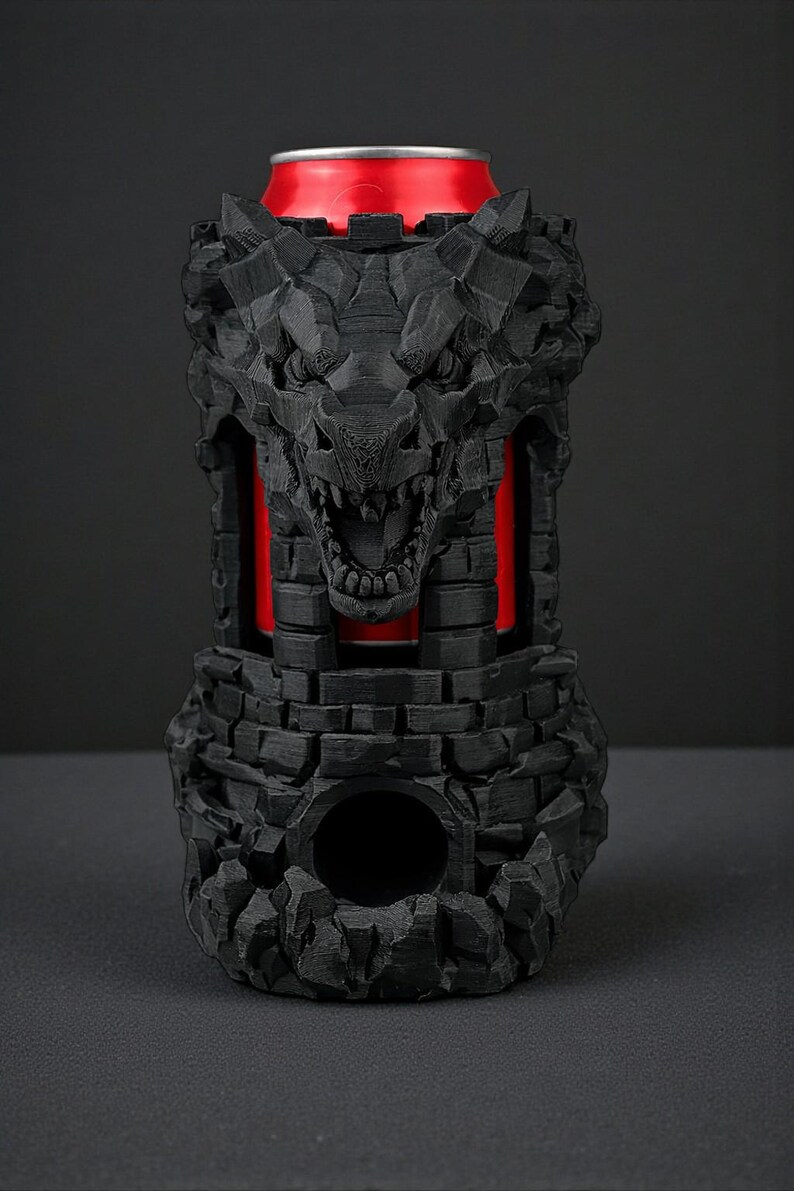 May include: A black, 3D-printed can cooler shaped like a castle with a snarling wolf's head. The cooler has a red interior, and a red can is visible inside. The design features a stone-like texture.
