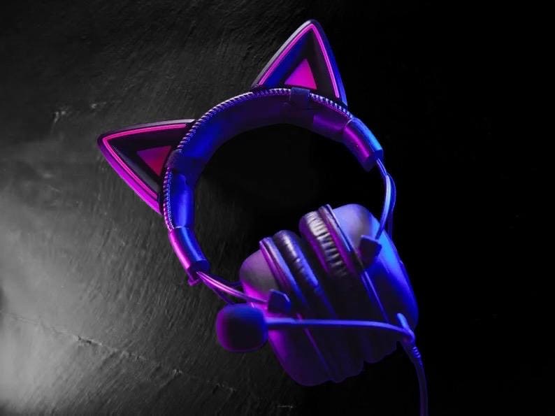May include: Purple and pink cat ear headphones with a microphone. The headphones have a black headband and earcups.