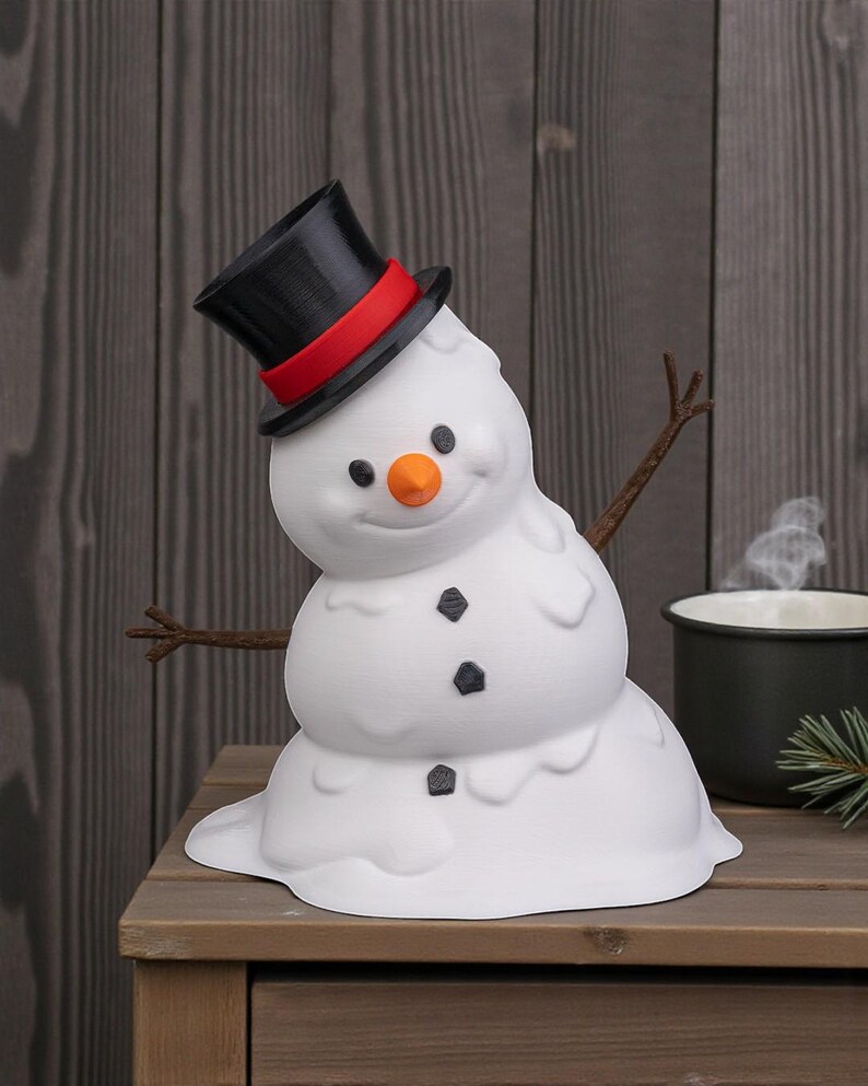 May include: A novelty white snowman ornament with a black top hat and red band, orange nose, and black button features. The snowman has twig arms and a melting design. It sits on a wooden surface.