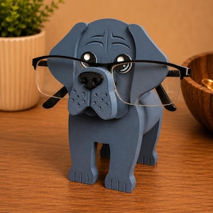 May include: A blue dog-shaped eyeglasses holder with black-framed glasses. The holder has a detailed face with a black nose and eye details. The dog is standing on four legs, and the glasses are resting on the nose.