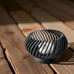 Pu&ograve; includere: Portacandele in metallo nero con un design a spirale. Il supporto ha una base rotonda e barre verticali curve, creando una struttura aperta. Una candela bianca &egrave; all'interno. Il portacandele &egrave; su una superficie di legno.
