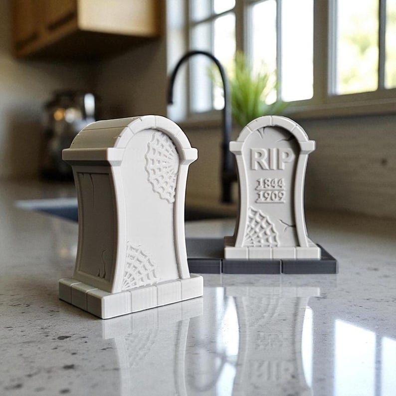 May include: Two gray, tombstone-shaped decorations. One features a spiderweb design, while the other has "RIP" and the years 1844 and 1909. These Halloween-themed decorations are perfect for adding a spooky touch to any space.