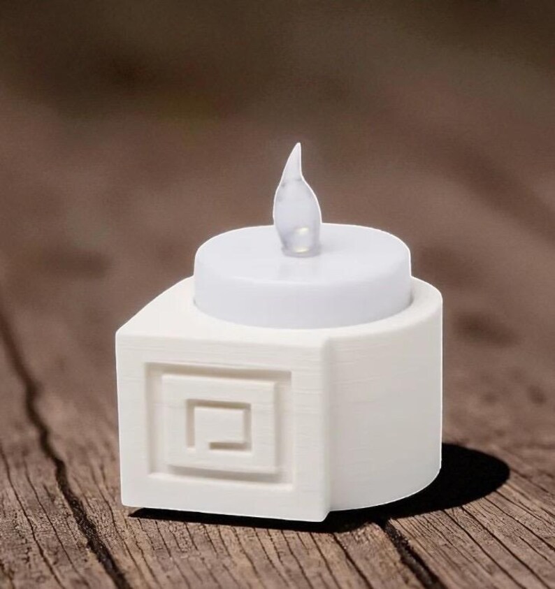 May include: A white LED candle with a realistic flickering flame. The candle sits atop a square base with a recessed geometric design. The candle is designed to look like a real candle.