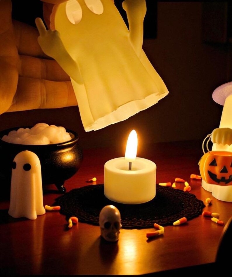 May include: A Halloween-themed display featuring a lit candle, a small skull, and a miniature ghost figure. A cauldron with white foam and candy corn are also present. A large ghost-shaped lamp is held above the scene.