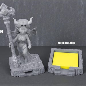 May include: A gray pen holder featuring a fantasy-themed figurine holding a staff, and a matching note holder with a yellow pad. The pen holder has the word "PEN" printed on it, and the note holder has the words "NOTE HOLDER" printed on it.