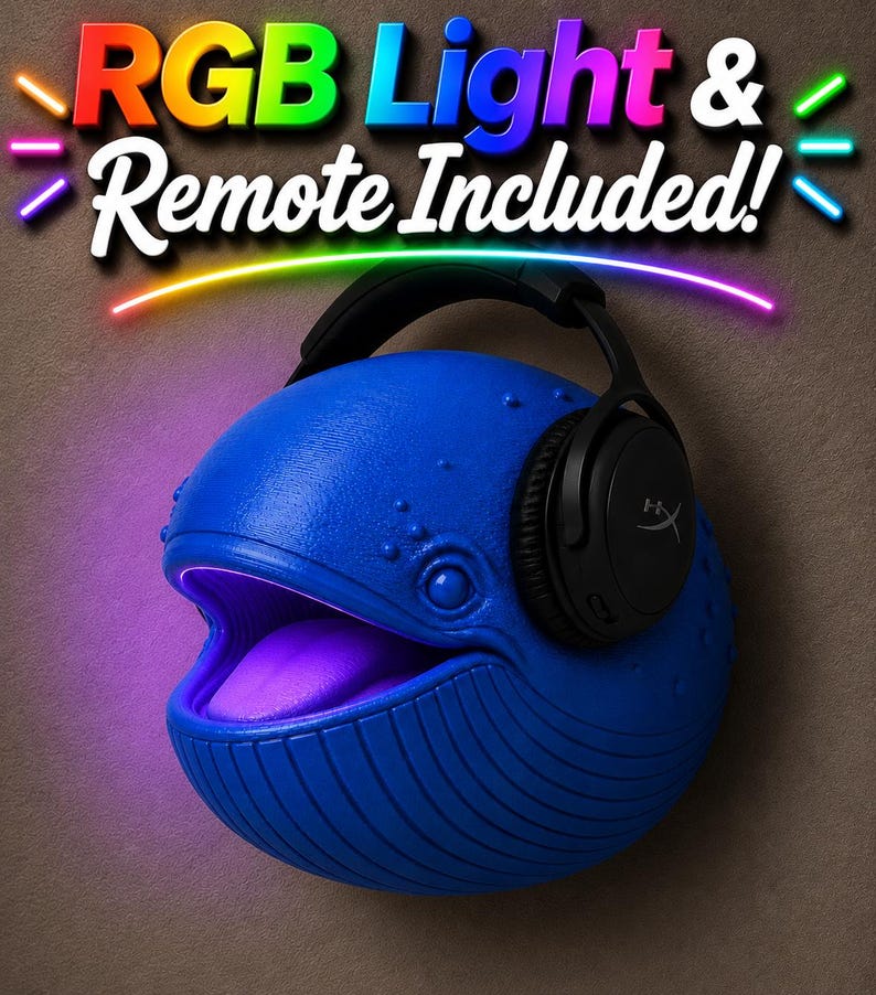 Op de afbeelding: Een blauwe walvisvormige lamp met een gloeiende paarse mond en een zwarte headset. De lamp heeft de tekst "RGB Light & Remote Included!" in kleurrijke letters. De lamp staat op een bruine achtergrond.