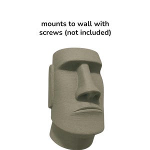 May include: A gray, textured Moai statue head, a replica of the iconic Easter Island sculptures. The statue has a prominent nose, defined facial features, and is designed to mount to a wall. The text in the image reads: mounts to wall with screws (not included).
