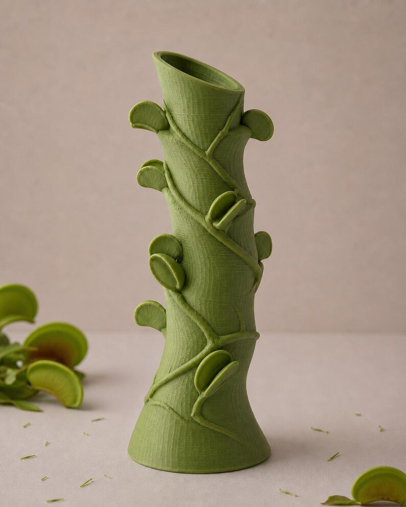 May include: A green, stylized vase with a textured surface, resembling a plant stem. The vase features leaf-like accents and winding vines, creating a botanical theme. The vase is approximately 10 inches tall.