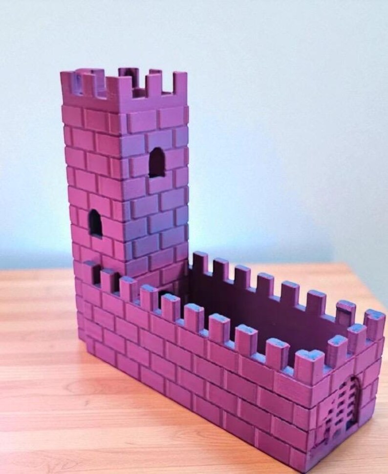 May include: A purple and pink castle-shaped planter with a tall tower and crenelated walls. The planter has a rectangular base and a small arched doorway. The brickwork is detailed, and the color gradient adds depth.