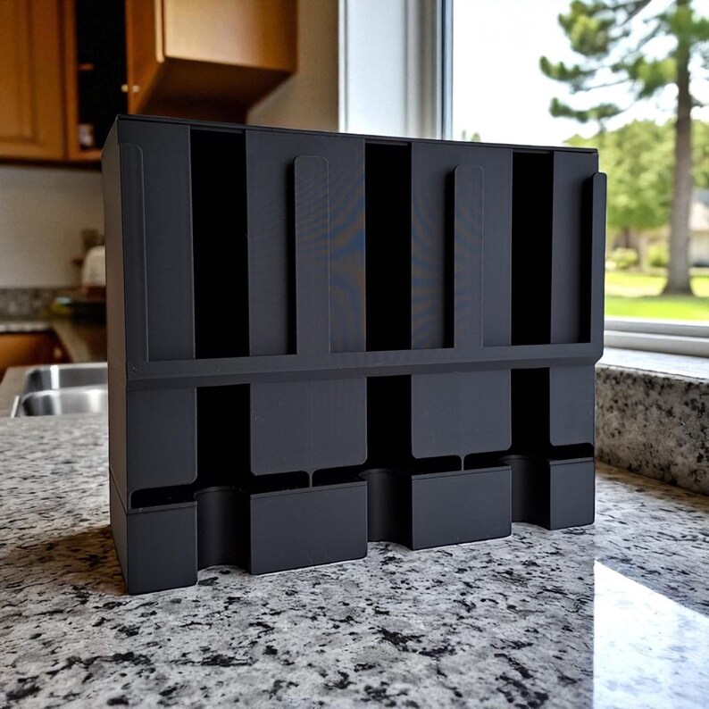 May include: A matte black organizer with multiple vertical slots and lower compartments. The organizer is designed to hold various items, likely for kitchen or office use. The structure is made of a solid, durable material.