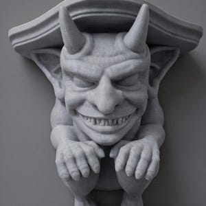 K&ouml;nnte beinhalten: Eine graue, 3D-gedruckte Gargoyle-Regalhalterung mit einem l&auml;chelnden Gesicht, H&ouml;rnern und ausgestreckten H&auml;nden. Das Regal hat eine dekorative Oberkante und ist f&uuml;r die Wandmontage konzipiert. Der Wasserspeier hat detaillierte Gesichtsz&uuml;ge und eine strukturierte Oberfl&auml;che.