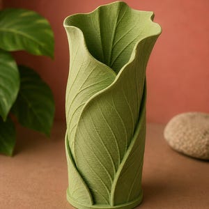 May include: A green vase with a leaf design. The vase is cylindrical with a flared top, and the exterior is textured to resemble overlapping leaves. The vase is approximately 8 inches tall and has a round base.