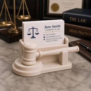 May include: A light-colored wooden business card holder with a gavel design. The holder displays a business card with the name "Jane Smith, Attorney at Law" and contact information. The background includes law books and a balance scale.