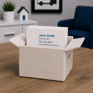 May include: A beige business card holder with a stack of white business cards. The cards display the name "Jane Smith", the title "REALTOR&reg;", a phone number, and an email address. The holder is on a wooden table.