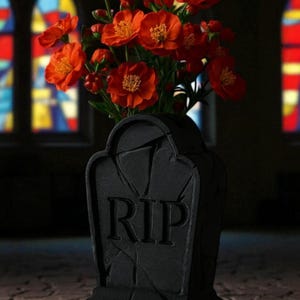 Puede incluir: Un jarrón negro con forma de lápida con las letras "RIP" talladas en la parte delantera, que contiene un ramo de vibrantes flores naranjas. Las flores tienen centros amarillos. El fondo presenta vidrieras.