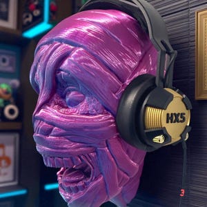 May include: A purple and blue sculpted head with bandages, wearing black and gold headphones. The headphones have the text "HXS5" on the earcups. The head has an open mouth and appears to be a mummy or monster.