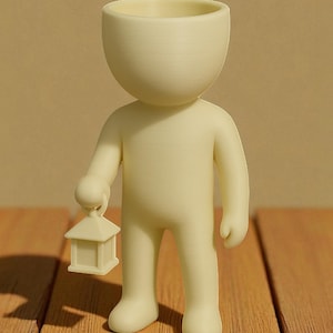K&ouml;nnte beinhalten: Cremefarbene Figur einer Person, die eine kleine Laterne h&auml;lt. Die Figur hat einen gro&szlig;en, offenen Kopf, und die Laterne hat die Form eines kleinen Hauses. Die Figur steht auf einer Holzoberfl&auml;che.