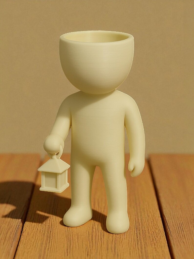 K&ouml;nnte beinhalten: Cremefarbene Figur einer Person, die eine kleine Laterne h&auml;lt. Die Figur hat einen gro&szlig;en, offenen Kopf, und die Laterne hat die Form eines kleinen Hauses. Die Figur steht auf einer Holzoberfl&auml;che.