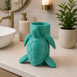 May include: A teal-colored toothbrush holder shaped like a turtle. The turtle is attached to a cylindrical holder. The holder is on a bathroom countertop with a sink, faucet, and soap dispenser in the background.
