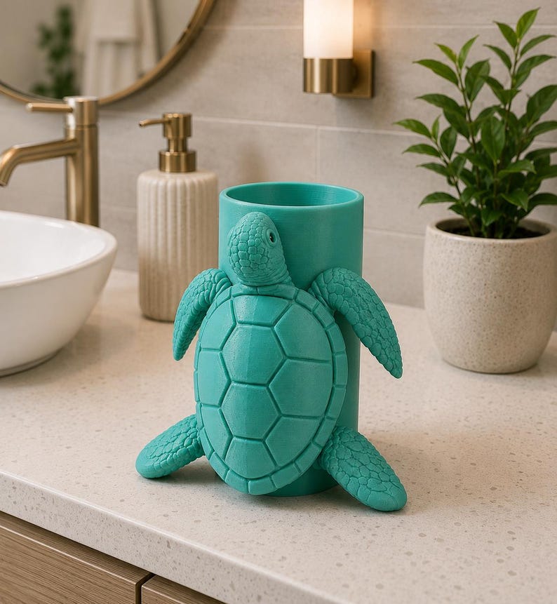 May include: A teal-colored toothbrush holder shaped like a turtle. The turtle is attached to a cylindrical holder. The holder is on a bathroom countertop with a sink, faucet, and soap dispenser in the background.